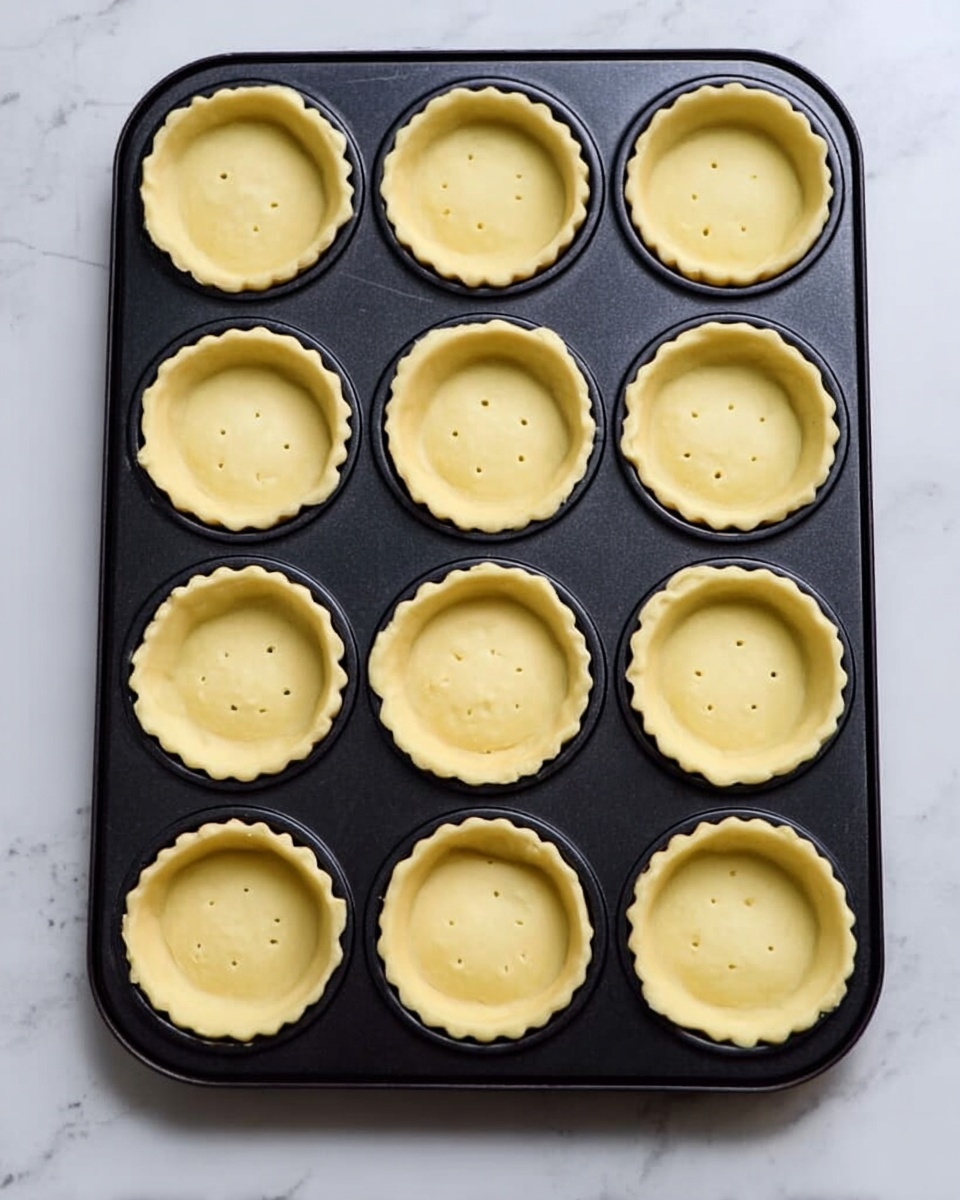 Several small puff pastry tarts sit on a white marbled surface covered with parchment paper, arranged with some close to the camera and others farther away. Each tart has three visible layers: a golden-brown, flaky puff pastry base with a rough texture and slightly raised edges, a smooth and creamy pale yellow cheese layer, and on top, a glossy layer of caramelized onions that are light to dark brown, soft and slightly translucent. Tiny green herb sprigs are scattered on a few tarts, adding a fresh touch. Crumbs and small bits of caramelized onion are scattered around the tarts on the parchment paper. Photo taken with an iphone --ar 4:5 --v 7