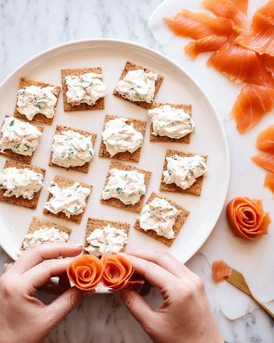 A white plate holds 16 small square crackers topped with a thick layer of white cream cheese mixed with small bits of pink and green herbs. The crackers are arranged in rows, almost filling the plate. In the foreground, a woman's hands are holding and shaping thin slices of orange smoked salmon into small rose shapes. To the right side on a white marbled surface, extra slices of smoked salmon lie flat with some pieces slightly torn. photo taken with an iphone --ar 4:5 --v 7