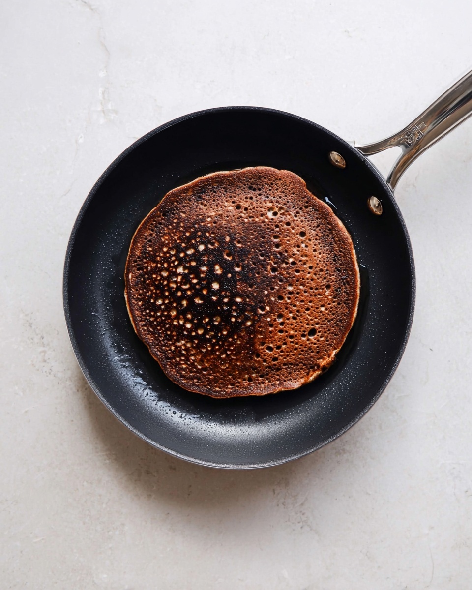 A stack of seven dark brown chocolate pancakes sits on a white plate on a white marbled surface, with a large slice taken out from the right side to show the soft, moist texture inside. The top of the stack is covered in smooth, shiny dark chocolate sauce that drips down the sides slightly. A fork with a dark wooden handle is inserted into the top of the sliced portion, lifting part of the stack. The inside of each pancake has a rich, slightly crumbly texture with some chocolate bits visible. photo taken with an iphone --ar 4:5 --v 7