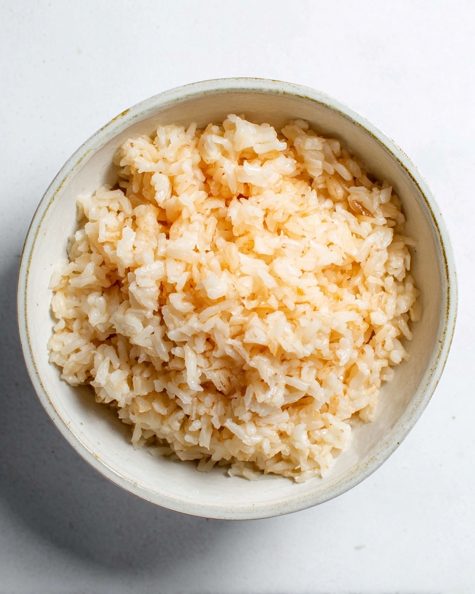A round white bowl sits on a white marbled surface, filled with one layer of sticky cooked rice that is light brown and shiny, showing a soft and slightly clumped texture. The rice grains are plump and evenly spread inside the bowl with no other visible ingredients. The lighting highlights the rice’s glossy surface, making it look fresh and tender. Photo taken with an iphone --ar 4:5 --v 7