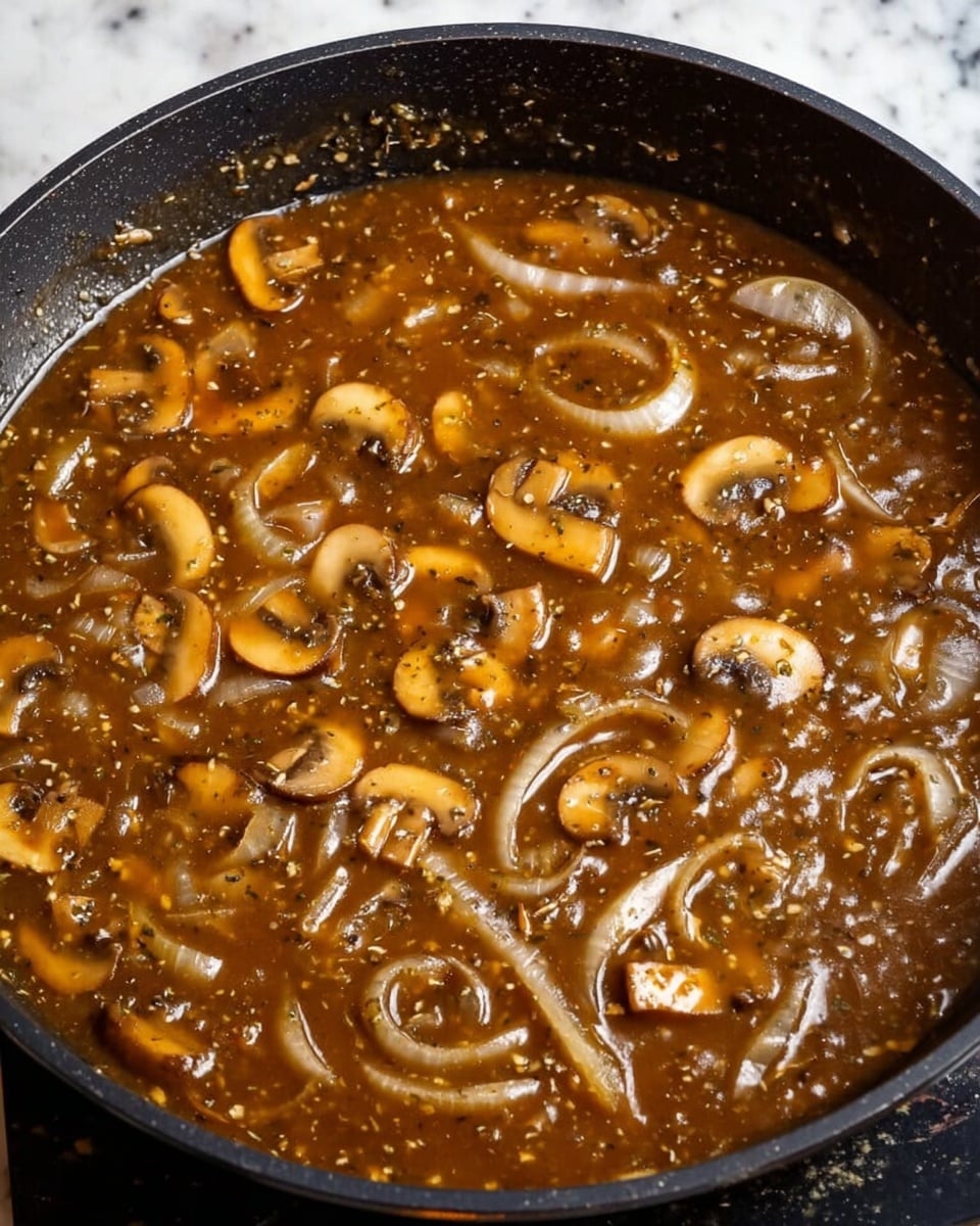 A white plate holds two main parts: on the left, there are dark brown cooked beef pieces covered with a glossy brown mushroom sauce and scattered with light brown mushroom slices and small bits of green parsley on top. On the right side of the plate, there is a mound of creamy white mashed potatoes with some light green herbs mixed in. The plate sits on a white marbled textured surface next to a blue and white striped cloth. photo taken with an iphone --ar 4:5 --v 7