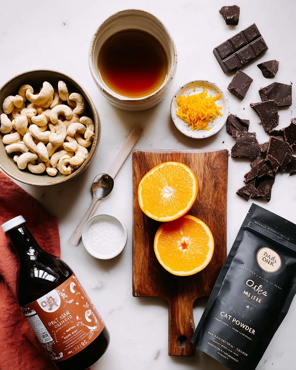 The image shows various ingredients arranged on a white marbled surface. In the center, there is a wooden cutting board holding two orange halves with bright orange flesh, a small white bowl with orange zest, and a spoon with white solid coconut oil. To the right of the board, dark chocolate pieces are scattered near a black bag labeled
