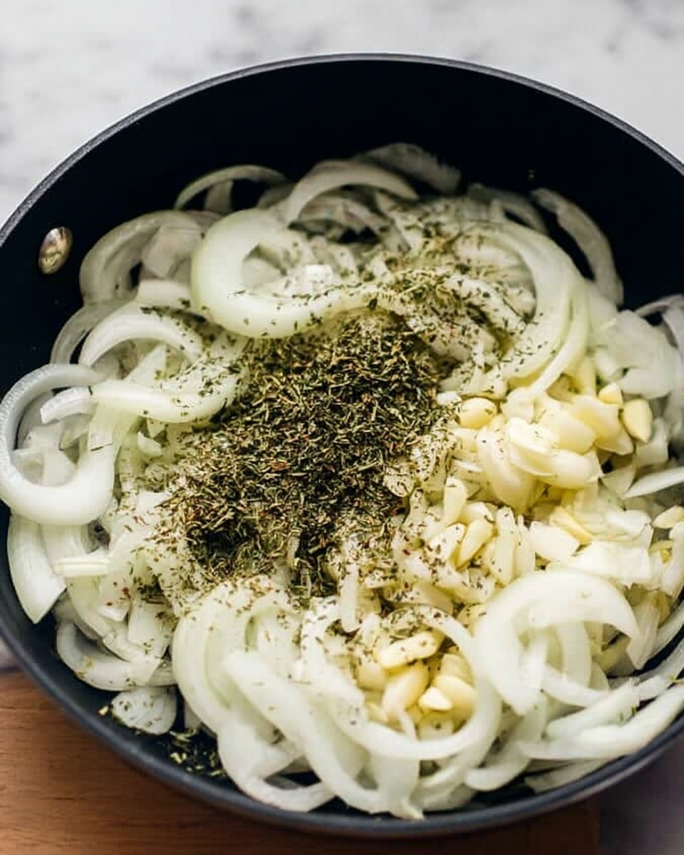 A black pan filled with thinly sliced white onions spread evenly across the surface, with small chunks of light-colored garlic mixed in. On top of the onions and garlic, there is a sprinkle of green dried herbs, creating a contrast in color. The pan is set on a white marbled surface. Photo taken with an iphone --ar 4:5 --v 7