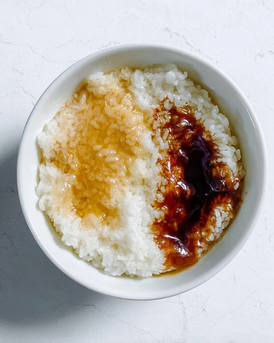 A white bowl filled with a layer of cooked white rice, topped with two different sauces. One sauce is light yellow and slightly translucent with a smooth texture on the left side, and the other sauce is dark brown and glossy, spreading over the right side of the rice. The bowl sits on a white marbled surface, showing subtle veins and texture. The lighting is natural and soft, highlighting the moist grains of rice and the shiny sauces. photo taken with an iphone --ar 4:5 --v 7