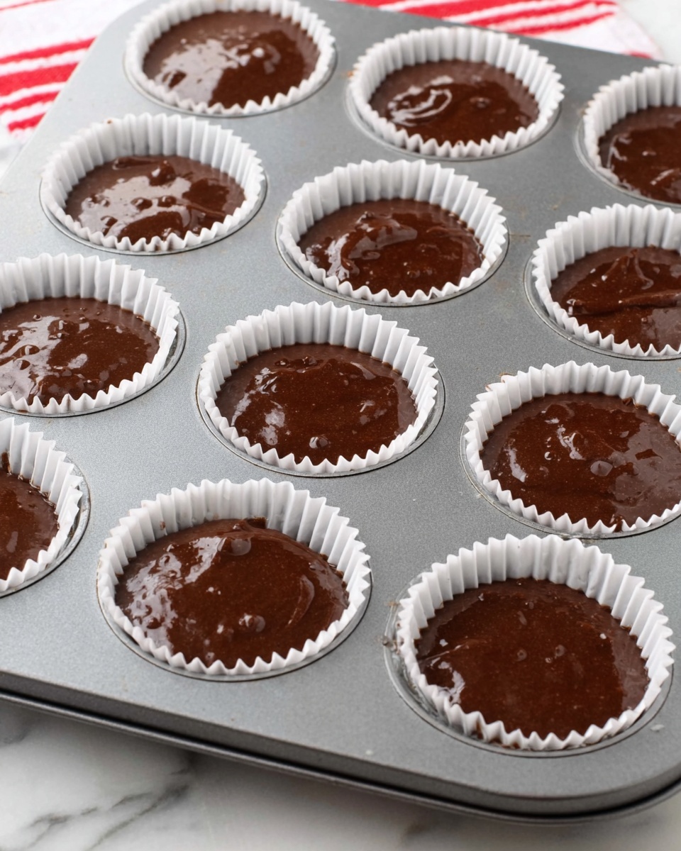 A chocolate cupcake sits in a red wrapper on a white marbled surface, with three layers visible: the bottom dark brown cake layer, a thick layer of light and fluffy chocolate frosting swirled on top, and thin dark chocolate drizzle lines on the frosting. Crushed white and red peppermint candy pieces are sprinkled all over the frosting. A gold metallic straw sticks out from the frosting at an angle on the right side. Surrounding the cupcake are white and red candy canes, a red glitter ball, and some scattered peppermint pieces. Photo taken with an iphone --ar 4:5 --v 7