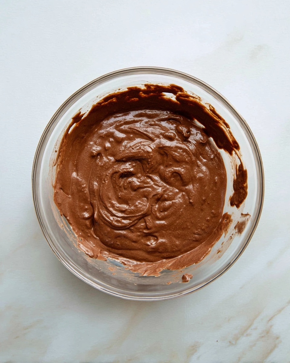 In a black nonstick frying pan with a silver handle, there is one round pancake in the center. The pancake is dark brown with a burnt look, showing many small holes and a rough texture on its surface. The edges of the pancake are uneven with a small curled part. The pan sits on a white marbled background, giving a clean and bright setting. photo taken with an iphone --ar 4:5 --v 7