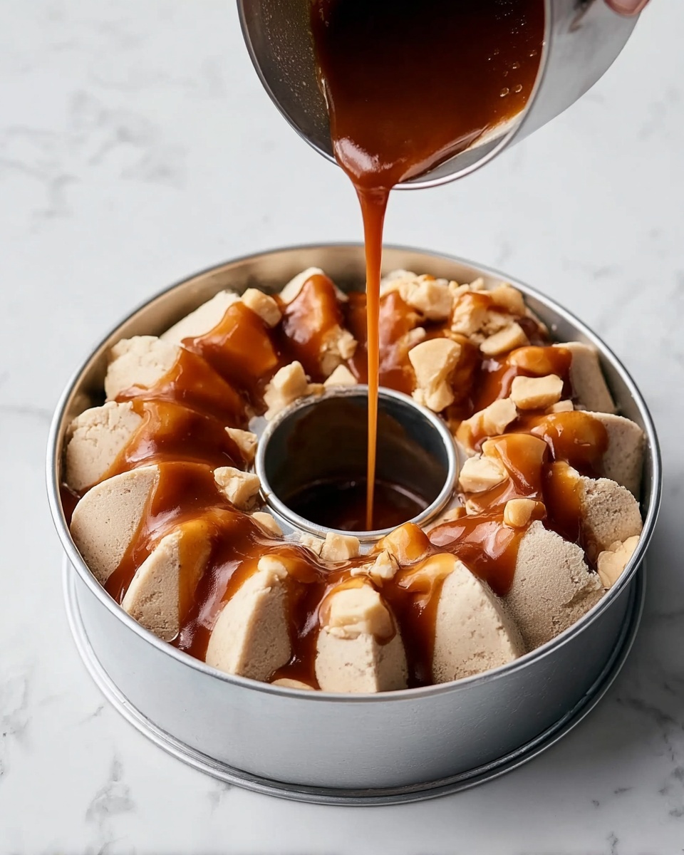 A bundt cake pan filled with thick, chunky pieces of pale beige dough arranged evenly around the center hole, topped with a glossy, rich brown caramel sauce being poured from a silver metal container held by a woman's hand, all placed on a white marbled surface. photo taken with an iphone --ar 4:5 --v 7