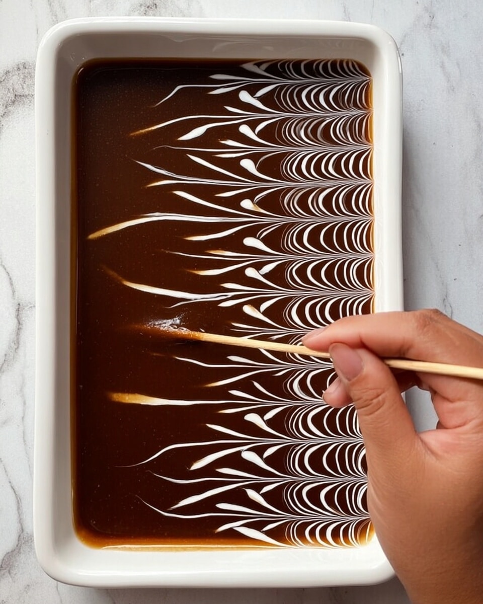 A single square piece of layered dessert sits in the center of a white scalloped plate. The dessert has three visible layers: a light beige bottom layer, a thick creamy middle layer soaked in milk, and a smooth caramel-brown top layer decorated with white swirled lines forming a wave pattern. The plate is placed on a white marbled surface with a gold-colored fork resting on its right side. In the background, there is a larger white ceramic baking dish filled with more of the same dessert, showing the same caramel top layer and white swirl pattern photo taken with an iphone --ar 4:5 --v 7