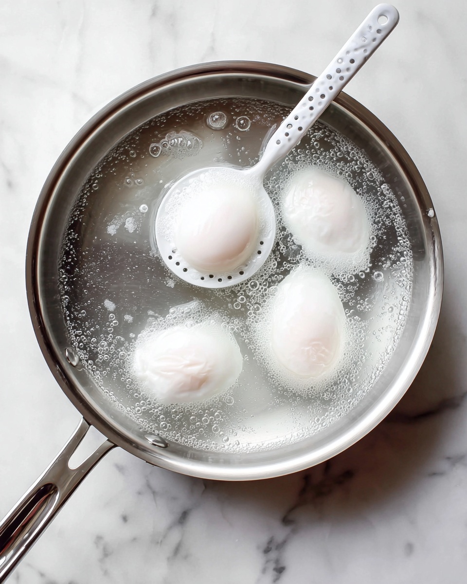 A stainless steel pan with four white poached eggs cooking in clear water, three eggs resting directly in the bottom of the pan while one egg is lifted by a perforated white spoon with a white handle, revealing its smooth, soft white surface and slight round shape. The pan is placed on a white marbled surface, and some small bubbles float around the eggs in the water, adding subtle texture. The overall look is clean and simple with a soft, light tone. photo taken with an iphone --ar 4:5 --v 7
