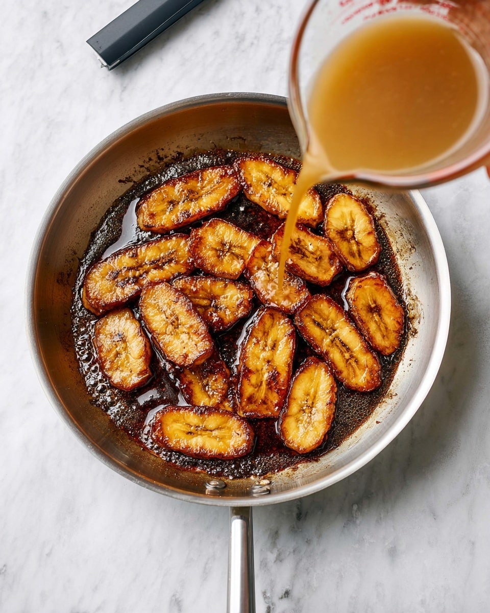A silver frying pan filled with about ten golden brown plantain slices, arranged in a single layer covering the bottom of the pan. The plantains have a shiny glaze, and they sit in a dark bubbling sauce that spreads evenly across the pan’s base. A woman's hand is seen pouring a light brown liquid from a clear measuring cup into the sauce. The pan rests on a white marbled surface, and a long black and gray lighter is placed near the top edge of the frame. Photo taken with an iphone --ar 4:5 --v 7