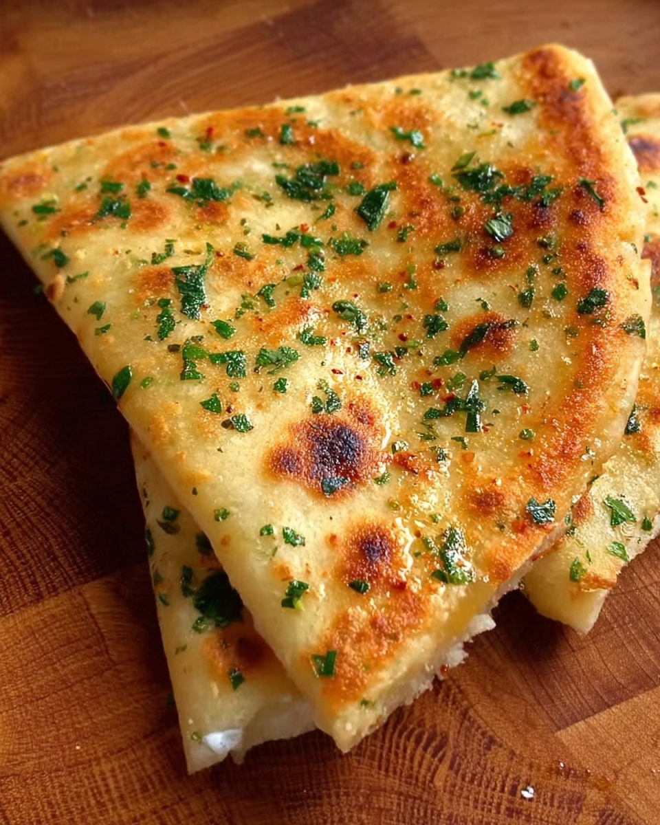 A close-up of a folded golden-brown flatbread with a slightly crispy texture, sprinkled with green herbs like chopped parsley and possibly some chili flakes on top. The flatbread has small browned spots and shines with a light layer of oil or butter, resting on a wooden surface with visible grain patterns. The edges are soft but show a slight crispiness, and some white filling is slightly visible oozing from one side. Photo taken with an iphone --ar 4:5 --v 7