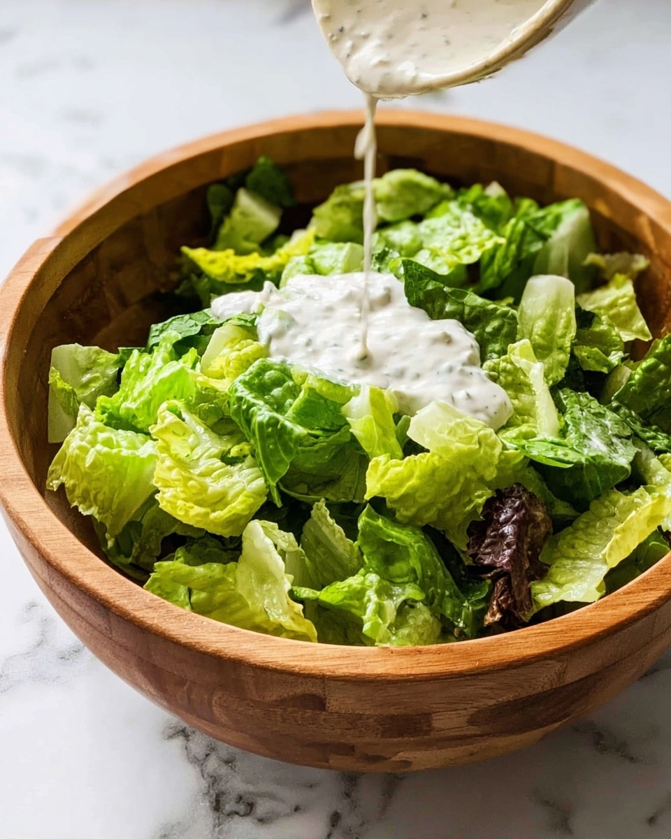 A wooden bowl filled with a mix of chopped green lettuce leaves showing different shades of bright and dark green. A dollop of creamy white dressing is being poured over the salad, sitting on top of the leaves. The bowl is placed on a surface with a white marbled texture, adding a clean look. The image captures the fresh texture of the lettuce and the smooth sauce on top. photo taken with an iphone --ar 4:5 --v 7