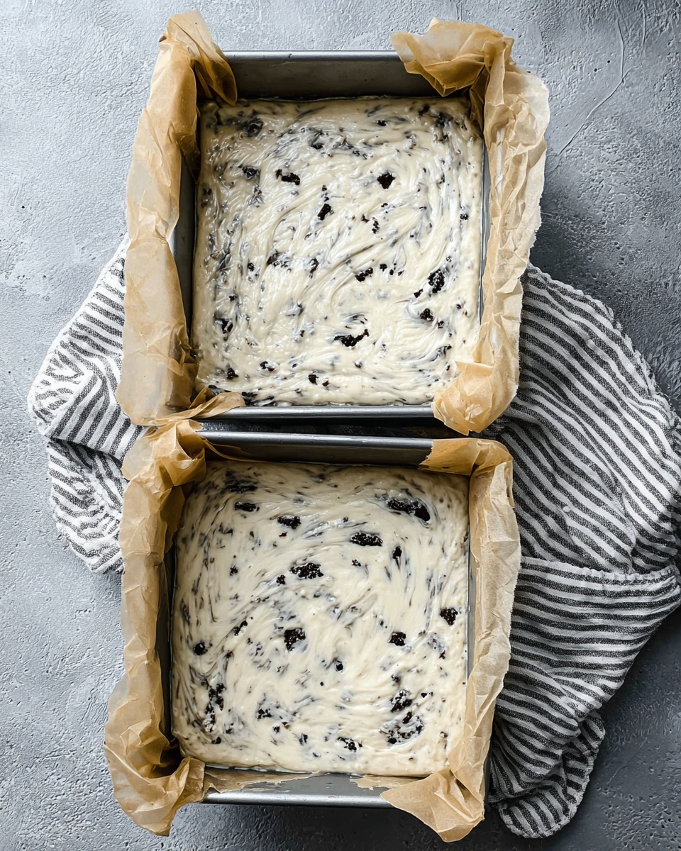 A white plate holds a pile of square-shaped white fudge pieces filled with dark cookie chunks inside. Each piece has a smooth, creamy texture with bits of cookie mixed throughout and crumbs sprinkled on top. Some cookie halves are used as decoration on the top layer. Around the fudge, there are whole dark sandwich cookies placed on the plate. The plate sits on a white marbled surface. photo taken with an iphone --ar 4:5 --v 7