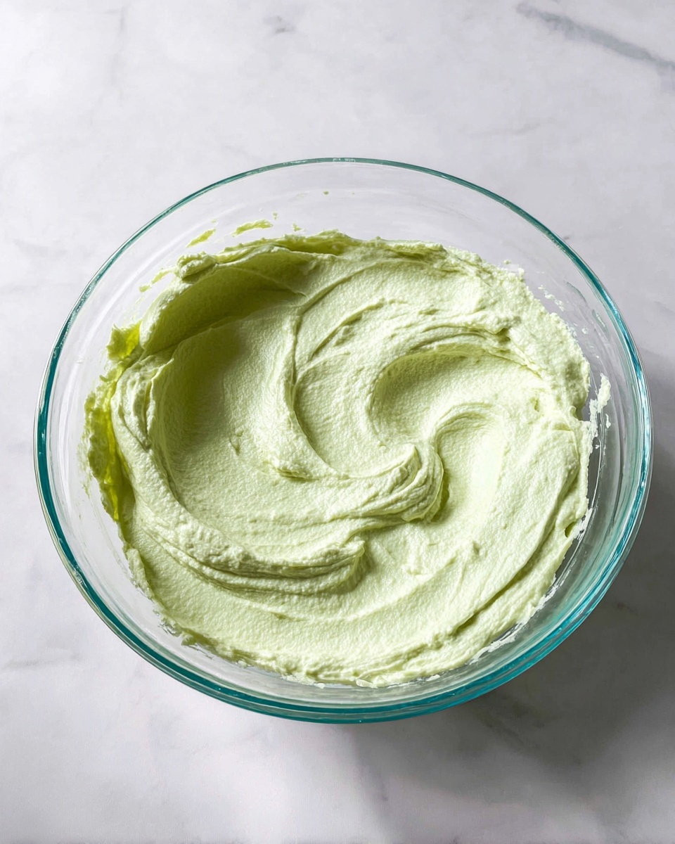 The image shows a close-up of a woman's hand holding a small, crisp pastry shell with a golden brown textured surface. The end of the pastry is dipped in melted dark chocolate and coated with bright green crushed pistachio nuts, creating a colorful and crunchy ring. In the first part, the pastry is dipped into a small white ceramic bowl filled with the same green crushed pistachios. In the second part, another woman's hand is holding the pastry while a third woman's hand uses a piping bag with light green filling being squeezed neatly into the hollow shell. The background and surface are white marble texture, highlighting the vivid colors of the treat. photo taken with an iphone --ar 4:5 --v 7