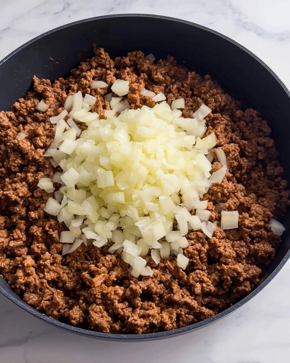 In a black pan, there is one layer of cooked, crumbled ground meat, brown in color with a slightly coarse texture, filling most of the pan's surface. On top, in the center, there is a pile of chopped onions, pale yellow and white, with a firm, fresh texture. The background is a white marbled surface. Photo taken with an iphone --ar 4:5 --v 7