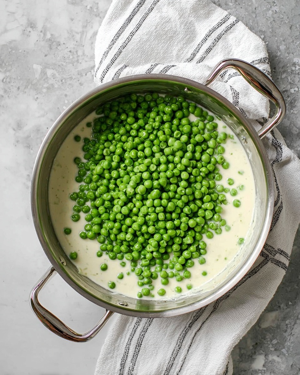 A white bowl with a slightly rough edge filled with bright green peas covered in a creamy white sauce. In the center, a square of yellow butter is melting, creating a shiny, smooth texture that blends with the sauce and peas around it. The bowl sits on a white marbled surface with a subtle light pattern. Photo taken with an iphone --ar 4:5 --v 7
