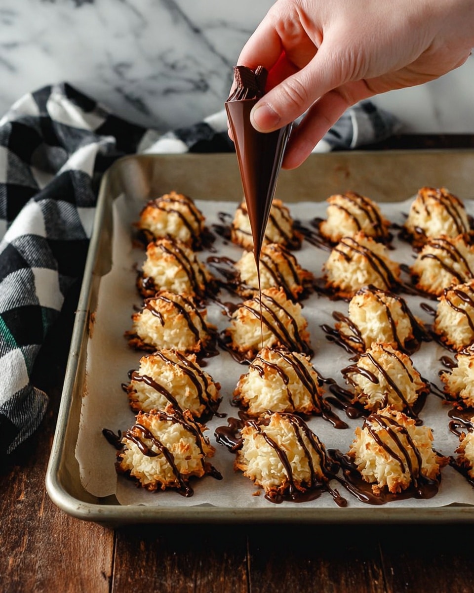 The image shows small round coconut treats with a light golden crust on the bottom and white, shredded coconut texture all over. Each treat is covered with thin, dark chocolate drizzled in a zigzag pattern on top, adding contrast to the white coconut. They are placed on a flat light brown surface, spaced evenly and slightly blurred in the background to focus on the main cluster in the front. photo taken with an iphone --ar 4:5 --v 7