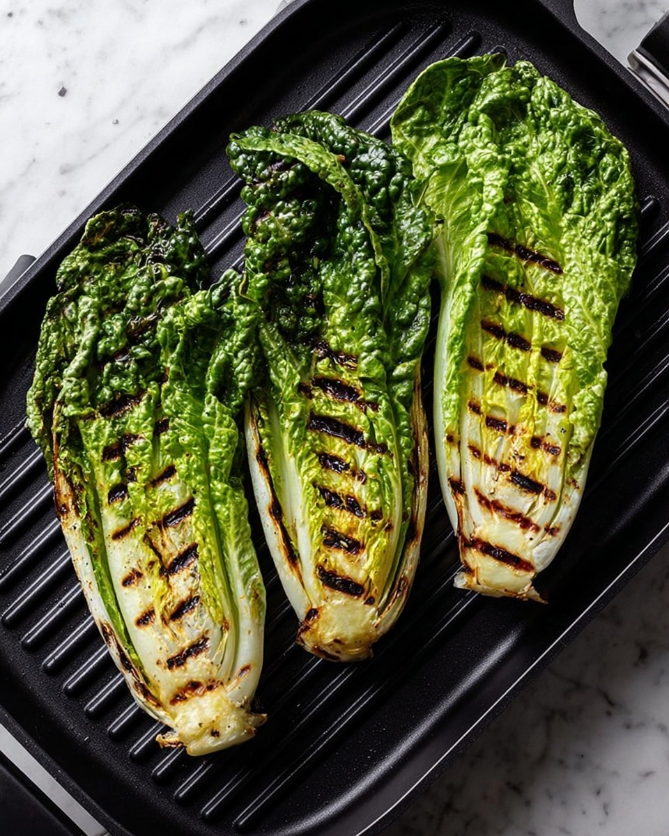 Three long romaine lettuce halves with dark green outer leaves and pale green inner leaves are placed side by side on a black grill pan. Each lettuce half has visible dark brown grill marks crossing parts of the leaves vertically, showing a light char on the edges and soft green texture beneath. To the right, a white plate partially enters the frame, holding a grilled romaine half with the same colors and marks. The background is a white marbled texture. photo taken with an iphone --ar 4:5 --v 7