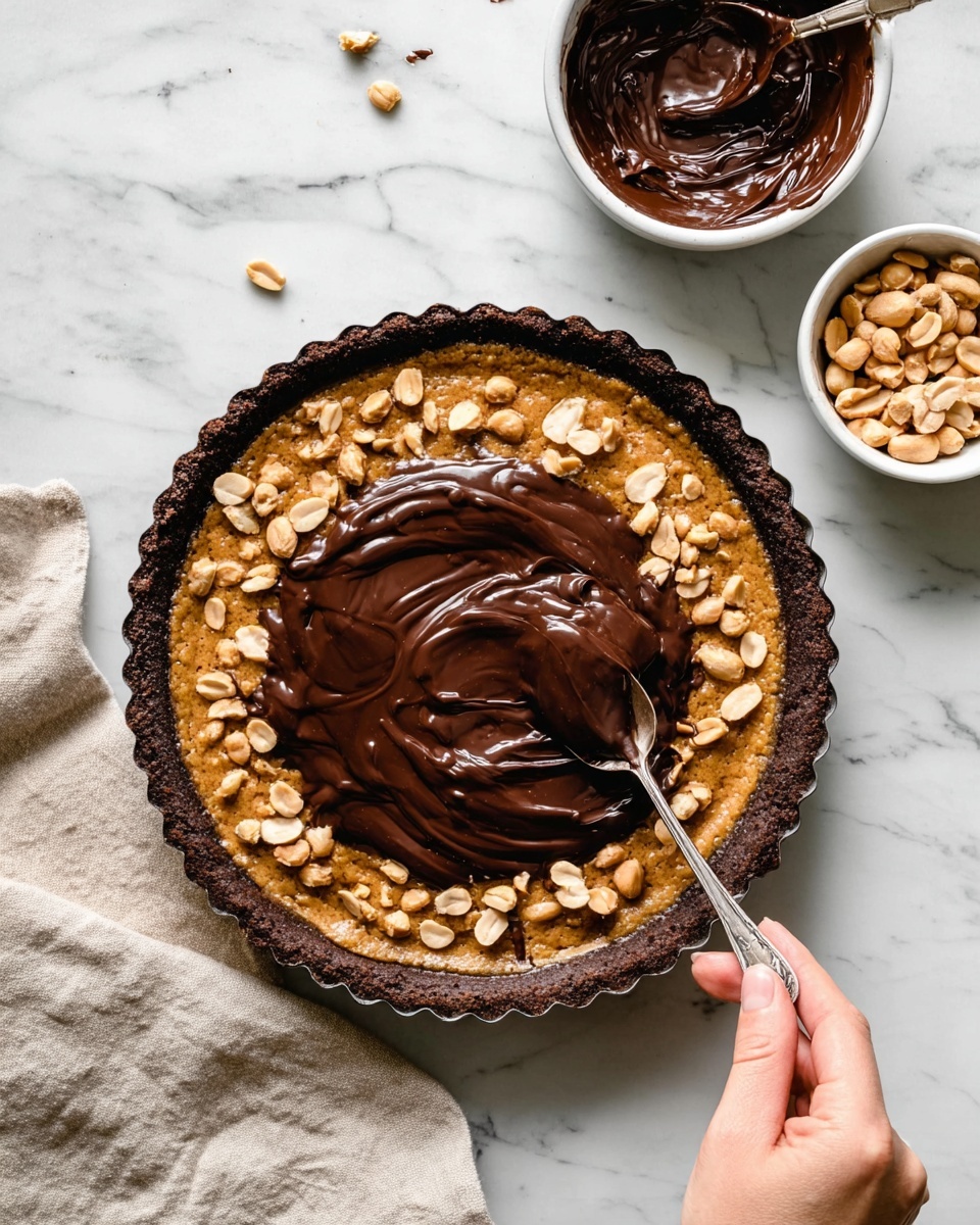 A round dessert tart with a dark brown crust and a golden brown filling that has visible pieces of light tan peanuts spread evenly throughout. On top of the tart, a thick layer of glossy, dark chocolate sauce is being spread with a silver spoon held by a woman's hand coming from the right side. To the upper right of the tart, there are two white bowls, one filled with melted dark chocolate and the other with whole peanuts. The background is a white marbled surface and a light beige cloth is placed on the bottom left corner of the image. Photo taken with an iphone --ar 4:5 --v 7