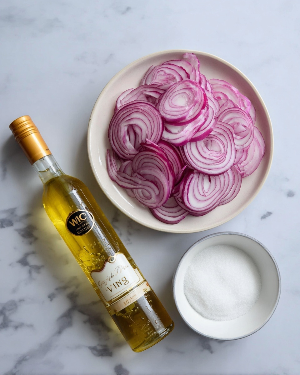 A white round plate filled with thin, circular slices of red onion layered loosely and showing their pale purple and white rings, next to a clear glass bottle with golden liquid labeled
