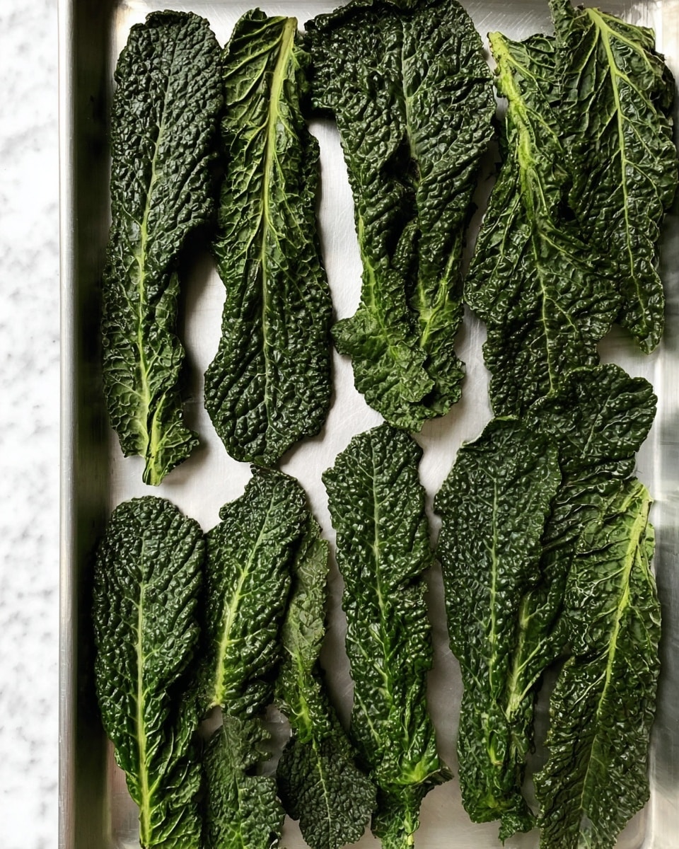 A silver tray filled with dark green kale leaves spread out in three vertical rows, each leaf showing a bumpy texture and visible veins. The leaves vary in size and shape, with some twisted edges, creating a pattern of deep greens and shadows on the tray's smooth surface. The background is white marbled texture. Photo taken with an iphone --ar 4:5 --v 7