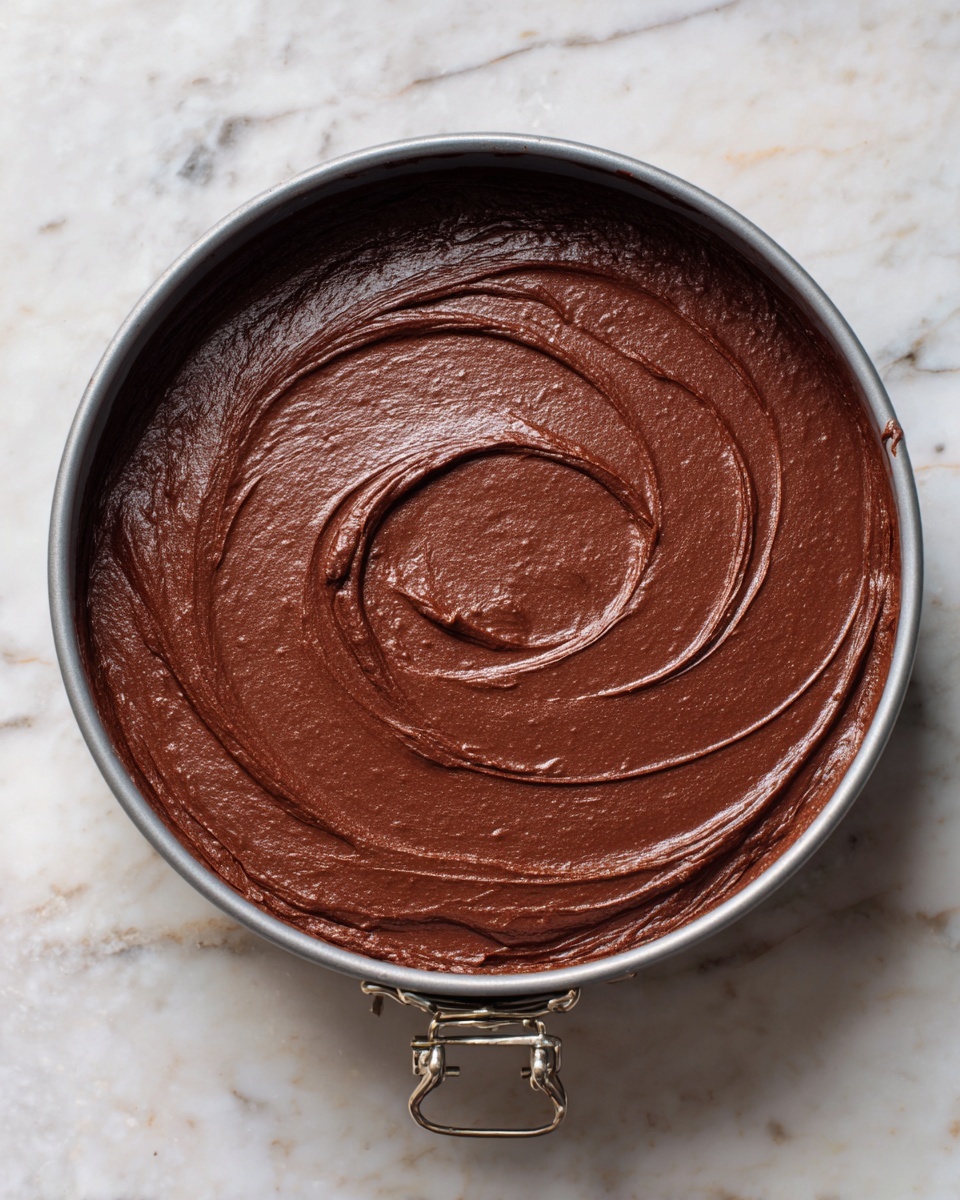 Flourless Chocolate Cake with Ganache and Fresh Berries Recipe 5 A rich chocolate cake with one slice taken out sits on a white cake stand. The cake has two visible layers: a thick, dense, dark brown bottom layer and a smooth, glossy layer of chocolate frosting on top. A large pile of fresh, bright red raspberries covers the center and part of the edges of the cake, some spilling over the sides. The cake stand is placed on a gray wooden surface with a soft pink cloth nearby, all set against a white marbled texture background. photo taken with an iphone --ar 4:5 --v 7