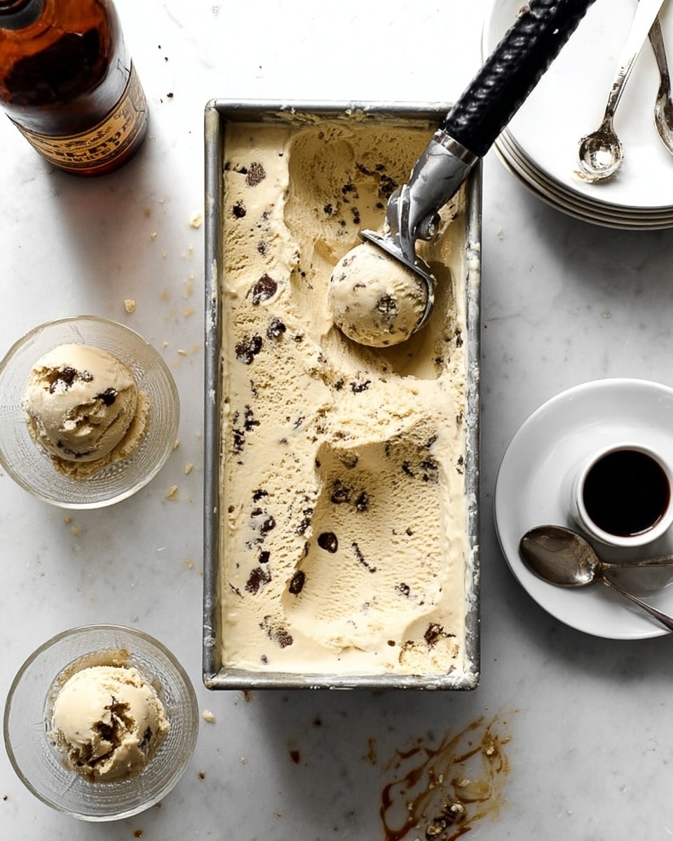 There are two clear glass dessert glasses each holding two scoops of light brown ice cream with small dark fruit pieces mixed in, placed on a white plate with two shiny dark chestnuts beside them; one glass has a small metal spoon resting on top of the ice cream, and in the background, another similar glass with two scoops of the same ice cream sits alone on a white marbled surface, with a dark gray cloth partially visible. photo taken with an iphone --ar 4:5 --v 7