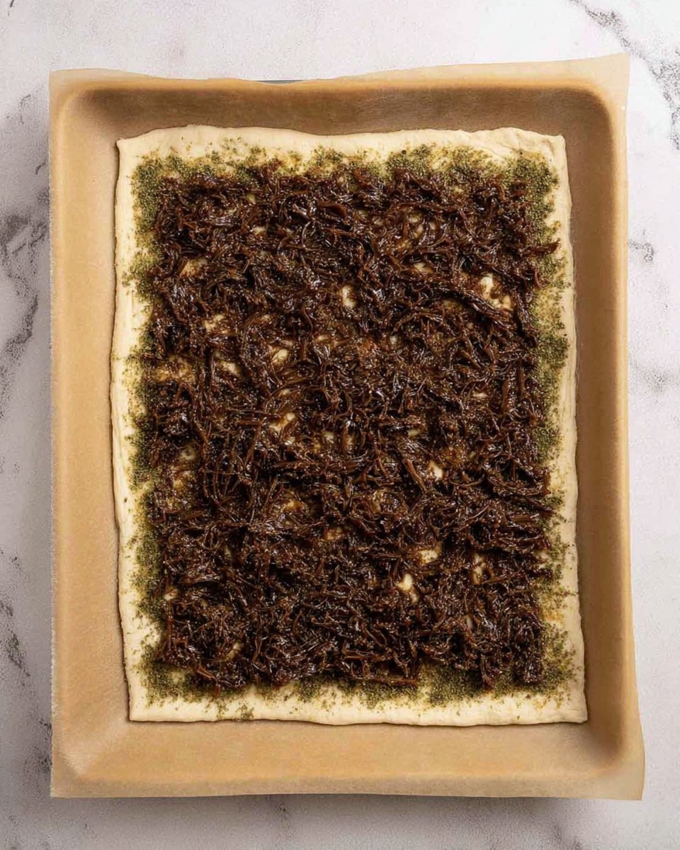 A square piece of pale dough lies flat on parchment paper inside a baking tray. It is topped with a thick, even layer of dark brown mixture that looks shredded and slightly moist. Around the edges of the mixture, a greenish herb seasoning is spread in a thin line close to the dough's border. The parchment paper has a light beige color, and the background is a white marbled texture. photo taken with an iphone --ar 4:5 --v 7