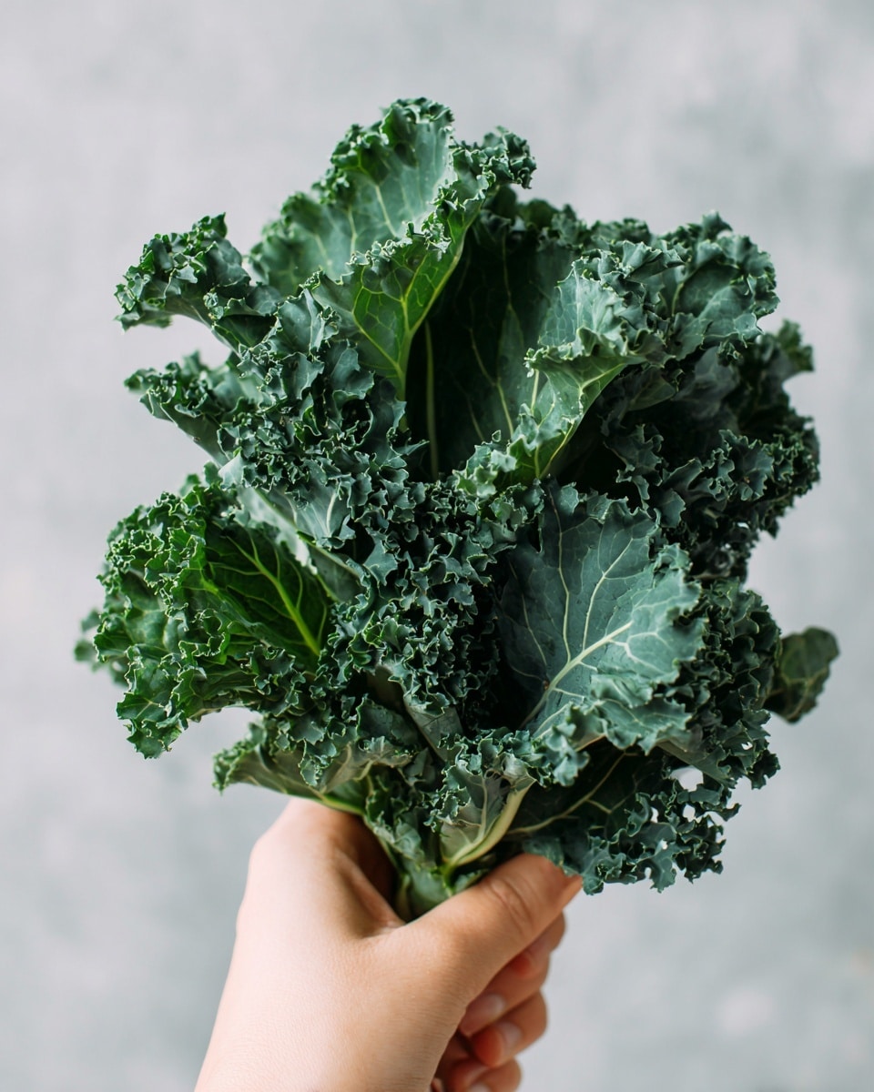 A close-up image shows a woman's hand gently holding a small bunch of dark green kale leaves. The kale has a ruffled texture with several layers of curled and wavy edges. The leaves are vibrant with visible veins and a mix of lighter and darker green shades. The background is a soft, light grey that contrasts with the rich green of the kale. photo taken with an iphone --ar 4:5 --v 7