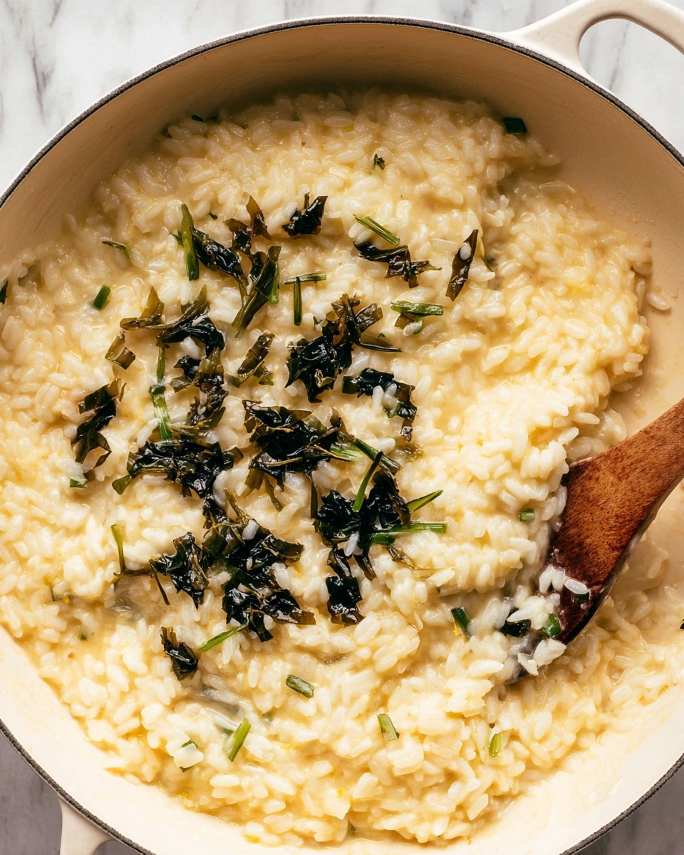 The image shows a close-up of a white pan with soft, creamy yellow risotto mixed with white grains of rice. On top, there are scattered pieces of dark green, slightly crispy cooked herbs or greens. A wooden spoon is partially visible on the right side, stirring the risotto. The pan sits on a surface with a white marbled texture, providing a clean and simple background. photo taken with an iphone --ar 4:5 --v 7