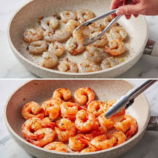 The image shows a close-up of a white plate filled with linguine pasta layered with plump shrimp and small pieces of red tomato sauce. The pasta strands are pale yellow and smooth, mixed with the orange-red sauce that lightly coats the shrimp and noodles. Fresh green chopped herbs are scattered unevenly over the dish, adding a fresh texture and bright contrast to the warm colors of the shrimp and pasta. Small red chili flakes are sprinkled on top, adding a hint of spice and color contrast. The plate rests on a white marbled surface. photo taken with an iphone --ar 4:5 --v 7