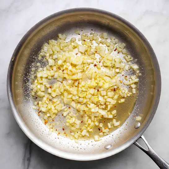 A close-up of a wooden spoon holding a heap of wet, dark red sun-dried tomato strips with a shiny, slightly wrinkled texture. Beneath the tomatoes is a shallow pool of golden olive oil created by the moist tomatoes. Around the tomatoes, there are scattered small pieces of white onions creating a border at the base. The whole setup is on a surface with a white marbled texture. photo taken with an iphone --ar 4:5 --v 7