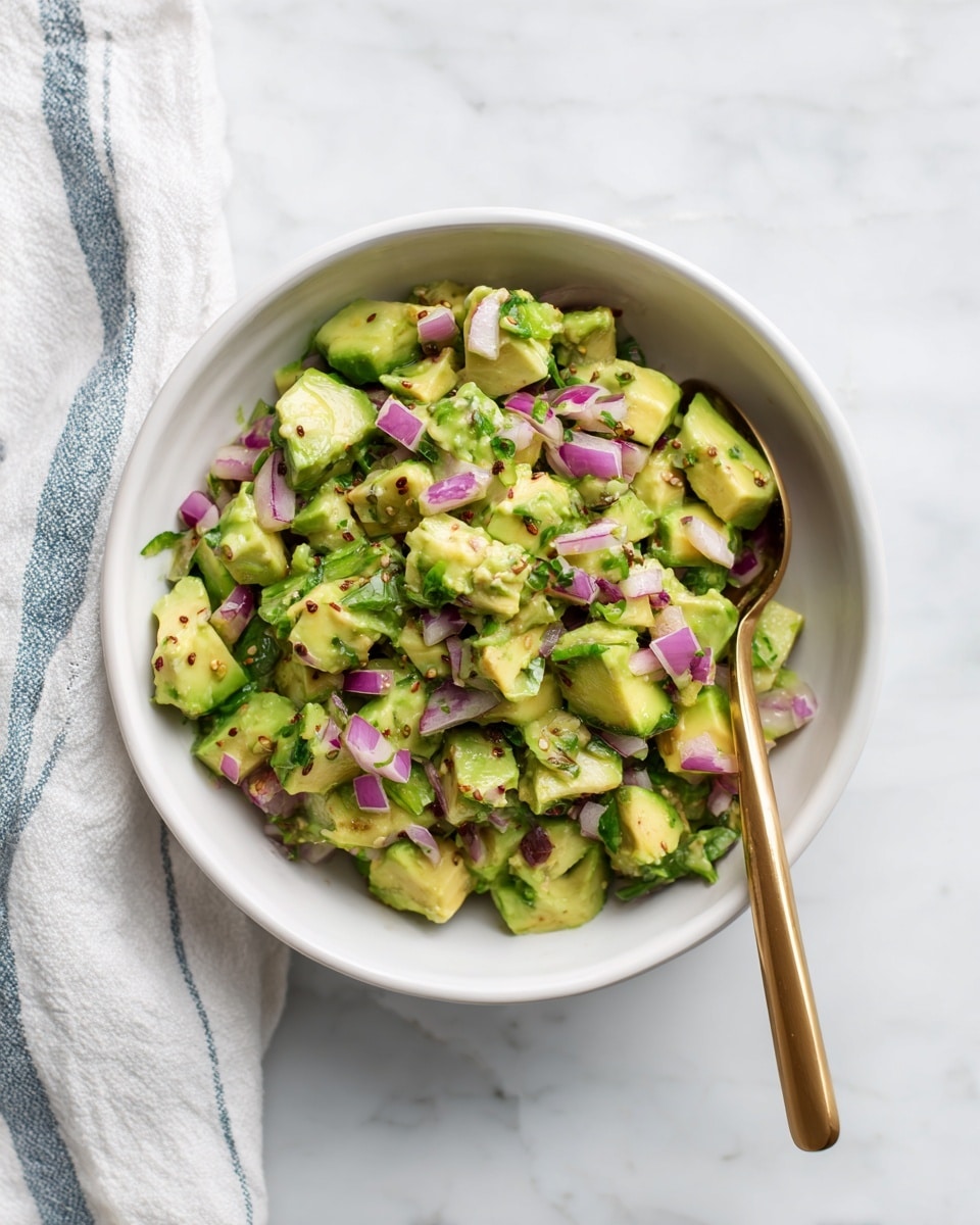In a white bowl on a white marbled surface, there is a mix of chopped avocado and small pieces of red onion. The avocado pieces are light green with a soft texture, scattered among the crunchy, purple-red onion bits. Black seeds are sprinkled on top, adding small dark accents to the mix. A golden spoon rests inside the bowl on the right side, partially covered by the mixture. A white cloth with thin blue stripes lies next to the bowl on the left side. photo taken with an iphone --ar 4:5 --v 7