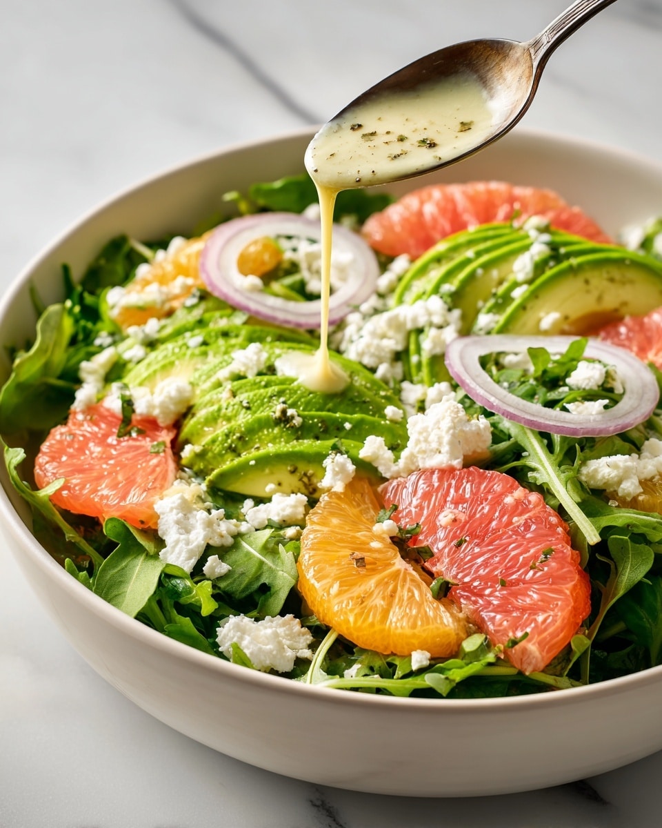 A fresh salad is shown in a white bowl on a white marbled surface, composed of green leafy arugula forming the base layer. On top, slices of avocado with light green flesh and dark green skin curve around orange segments that add vibrant color. Pink grapefruit pieces appear next to thin white onion rings scattered throughout. Crumbled white cheese is sprinkled over the salad. A spoon is held above, pouring creamy dressing that drips down onto the avocado and greens. photo taken with an iphone --ar 4:5 --v 7
