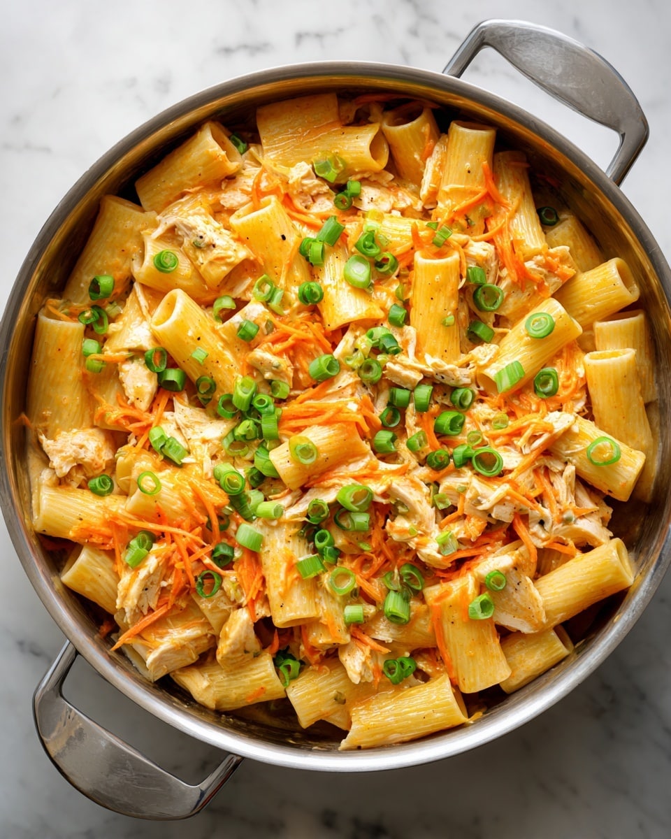The image shows a close-up of a white bowl filled with rigatoni pasta coated in a creamy orange sauce. The pasta is mixed with shredded pieces of cooked chicken and garnished with small, chopped green onions scattered on top. The bowl sits on a wooden surface with some green onions placed around it. The sauce looks thick and smooth, covering the pasta evenly, and the green onions add a bright contrast of color. Photo taken with an iphone --ar 4:5 --v 7