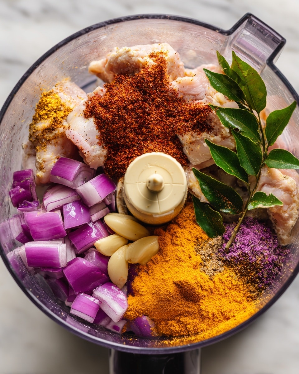Inside a clear food processor bowl, there are several layers of ingredients visible. At the bottom, there are light beige pieces of uncooked chicken, surrounded by scattered purple pieces of shallots and a few whole garlic cloves with a light golden-yellow color. On top of these, there are bright orange turmeric powder and reddish-brown chili powder sprinkled on the chicken, along with some sprigs of fresh green curry leaves resting on the side. The food processor blade stands upright in the middle, with chili powder piled on top of it. The whole setup is placed on a white marbled surface. photo taken with an iphone --ar 4:5 --v 7