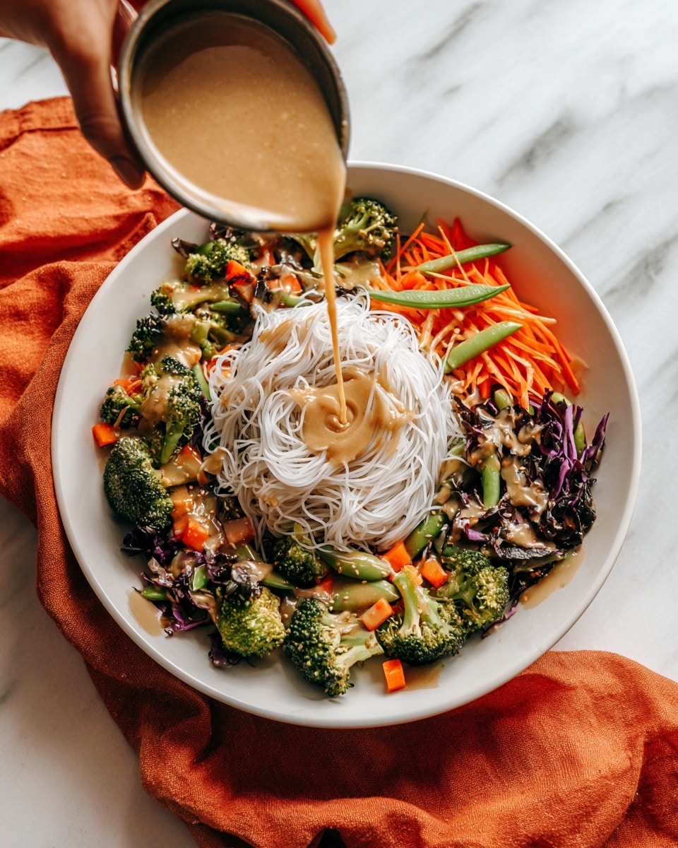 A white bowl holds a colorful dish with three main layers. The bottom layer is mixed green and purple vegetables, including broccoli florets, orange carrot slices, snap peas, and some dark leafy greens. On top of the vegetables is a nest of fine, white rice noodles arranged loosely in the center. A woman's hand is pouring a thick, light brown sauce over the rice noodles. The bowl sits on a white marbled surface with an orange cloth partially visible below it. photo taken with an iphone --ar 4:5 --v 7