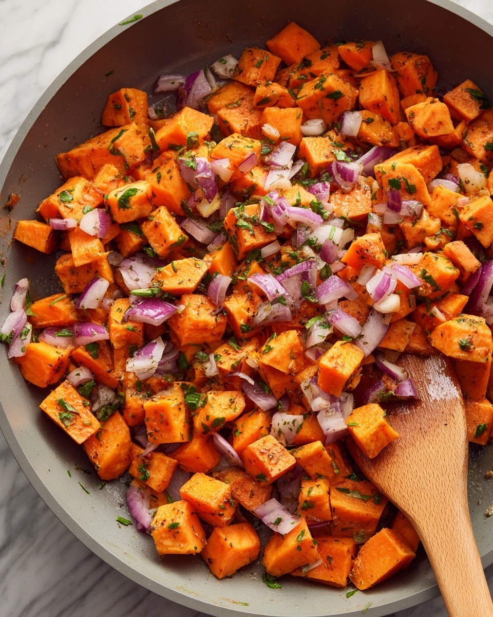 The image shows a close-up of a gray pan filled with small, evenly cut cubes of bright orange sweet potatoes mixed with bits of light purple onions. Small bits of herbs and garlic are scattered throughout the mixture. A wooden spatula is in the top right corner, stirring the ingredients. The background is a white marbled texture. photo taken with an iphone --ar 4:5 --v 7