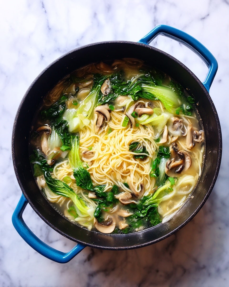 A black pot with blue handles holds a clear broth with thin light yellow noodles spread evenly in the center. Bright green leafy bok choy pieces and light beige mushrooms of different shapes are mixed through the soup, floating on the surface. The pot sits on a white marbled surface. The colors are fresh and natural, showing a simple, healthy soup. photo taken with an iphone --ar 4:5 --v 7