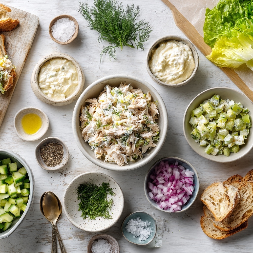 The image shows a sandwich cut into two stacked halves on a white plate with a white marbled surface underneath. The sandwich has three layers of light brown textured bread with visible holes, with two thick layers of creamy chicken salad mixed with small pieces of celery, red onion, and herbs between the bread slices. Below each chicken salad layer is a fresh green lettuce leaf. Some scattered bits of chicken salad and herbs are sprinkled around the plate. In the background, there is a blurred white marbled surface and part of another sandwich on a white plate. photo taken with an iphone --ar 4:5 --v 7