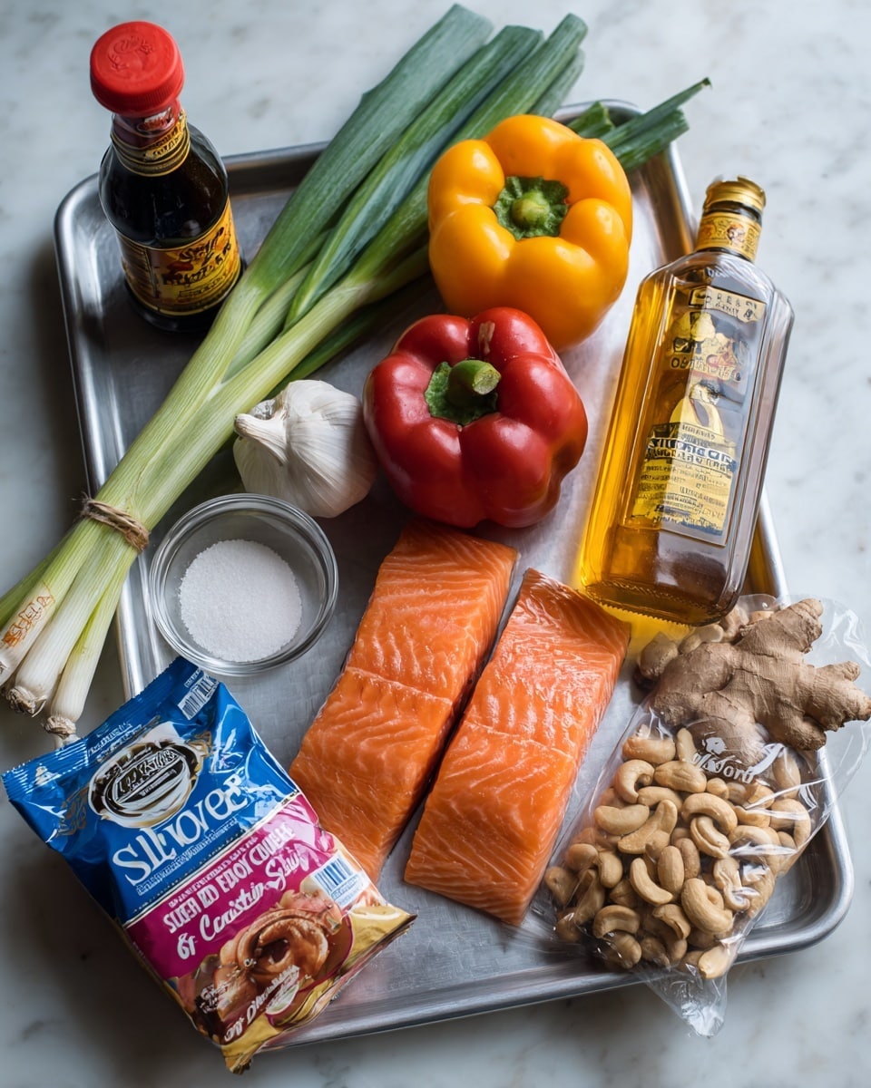 A metal tray on a white marbled surface holds fresh ingredients arranged neatly. On the left, green onions tied in a bundle stand upright, next to a dark glass bottle of light soy sauce with a red cap. In the middle, a pack of two salmon fillets with a blue label shows bright orange fish with white lines. Below that, a whole garlic bulb sits near a yellow bell pepper and a red bell pepper side by side. A small glass bowl of white powder is beside a tall clear bottle of golden cider vinegar with a yellow label on the right. At the bottom, a bag of roasted salted cashews in pink and white packaging overlaps a bag of dark brown soft sugar with a red and blue