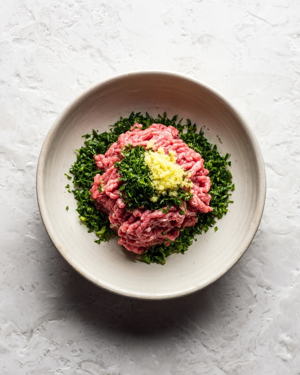 Inside a large white bowl, there is one layer of raw ground pink meat with a soft texture. On top, near the center, sits a layer of finely chopped dark green herbs, adding a fresh contrast. Below the herbs and slightly spread around them, there is a small mound of pale yellow minced garlic. The bowl is placed on a white marbled textured surface. Photo taken with an iphone --ar 4:5 --v 7