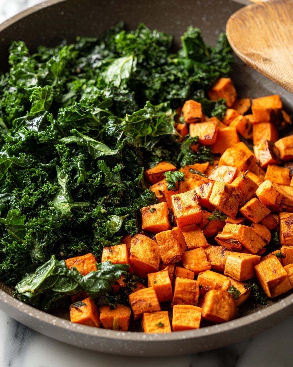 A close-up view of a gray pan filled with sautéed vegetables. The bottom layer consists of small, soft orange cubes, likely sweet potatoes, with a few specks of herbs visible. On top is a layer of dark green kale leaves, slightly wilted but still adding texture with some leaves showing a wrinkled surface. The scene is set on a white marbled surface, with part of a wooden spatula visible on the upper right side. The colors contrast well, highlighting the bright orange and deep green tones. photo taken with an iphone --ar 4:5 --v 7
