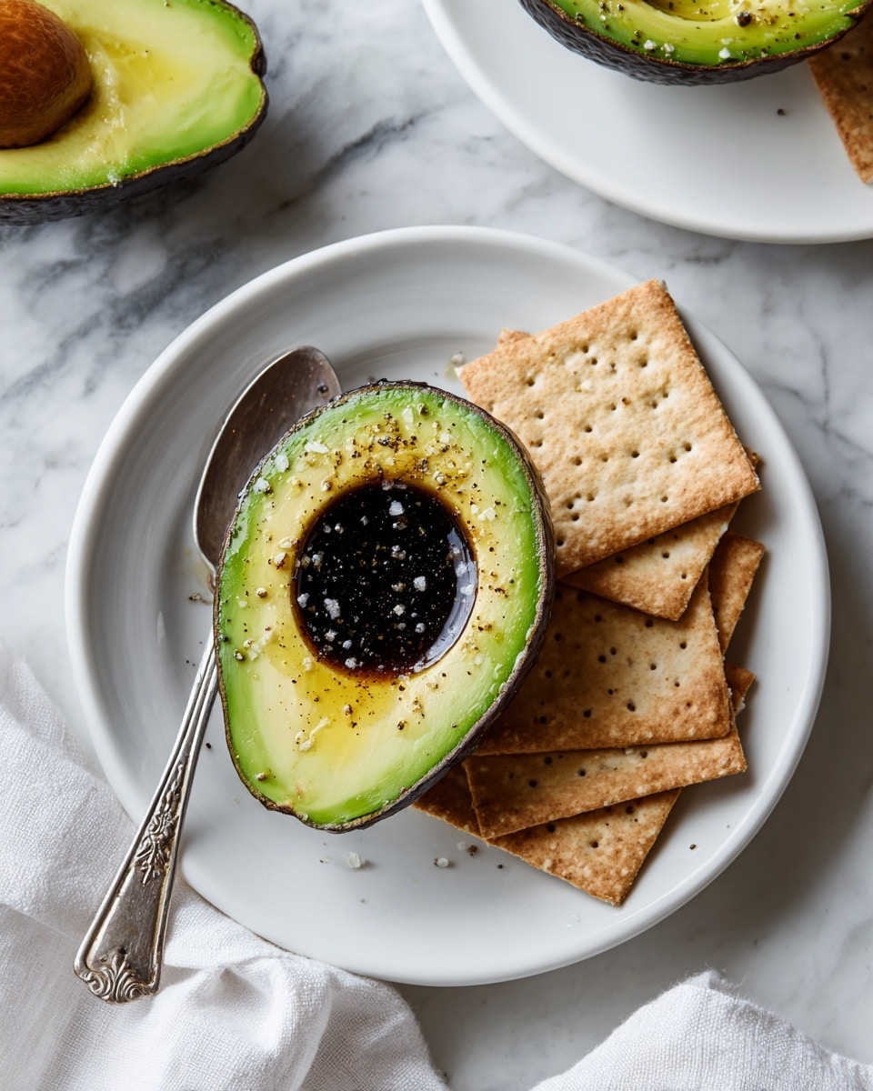 On a white plate with ridged edges, there is one halved avocado with its green flesh soft and creamy, topped with small white seeds and dark brown sauce drizzled over it, sitting next to a group of light brown square crackers arranged in a casual pile. A silver spoon with an ornate floral handle rests inside the avocado, showing some of the sauce and seeds on it. The plate sits on a white marbled textured surface, with a small bowl of the same white seeds visible in the upper left corner. Photo taken with an iphone --ar 4:5 --v 7