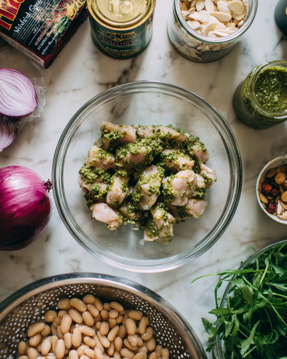 The image shows two parts: the top part features a clear glass bowl in the center containing raw chicken pieces coated with green pesto sauce, surrounded by various ingredients including a red onion on the left, a packet of baby arugula salad in the background, a tin of white cannellini beans behind the bowl, a small glass bowl with almond slivers to the right, a jar of creamy dressing, a jar of basil pesto, and fresh green parsley on the far right, all placed on a white marbled surface. The bottom part shows a colander with light beige cannellini beans being rinsed under running water in a kitchen sink. Photo taken with an iphone --ar 4:5 --v 7