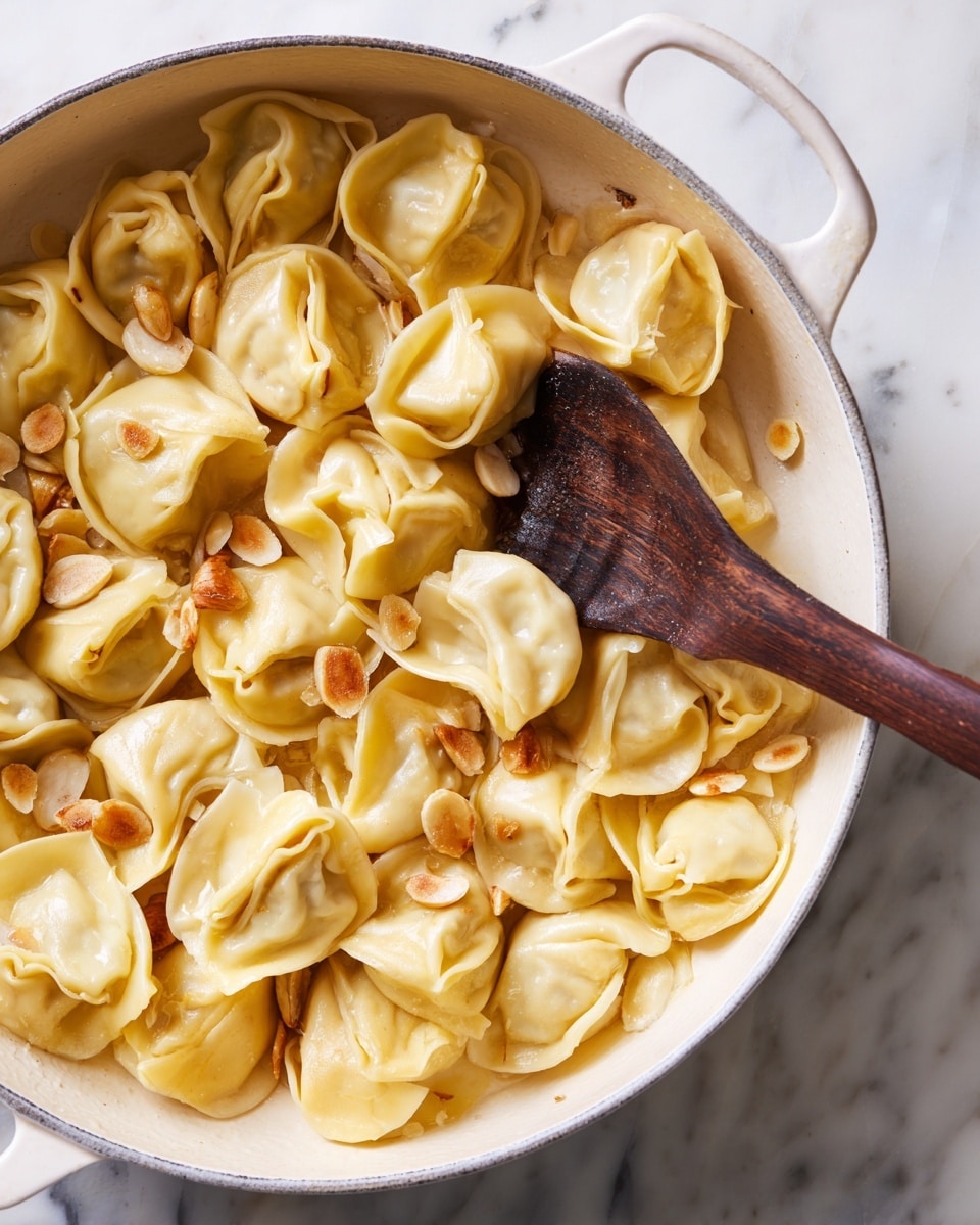 The image shows many dumplings cooking in a white pan on a white marbled surface. The dumplings are light yellow with soft, slightly wrinkled skins and folded edges. Scattered between and on top of the dumplings are small, thin slices of golden-brown cooked garlic. A dark wooden spoon rests inside the pan on the right side, touching the dumplings. The colors are warm and natural, with the dumplings' light yellow contrasting with the pan's white and the golden garlic slices. photo taken with an iphone --ar 4:5 --v 7