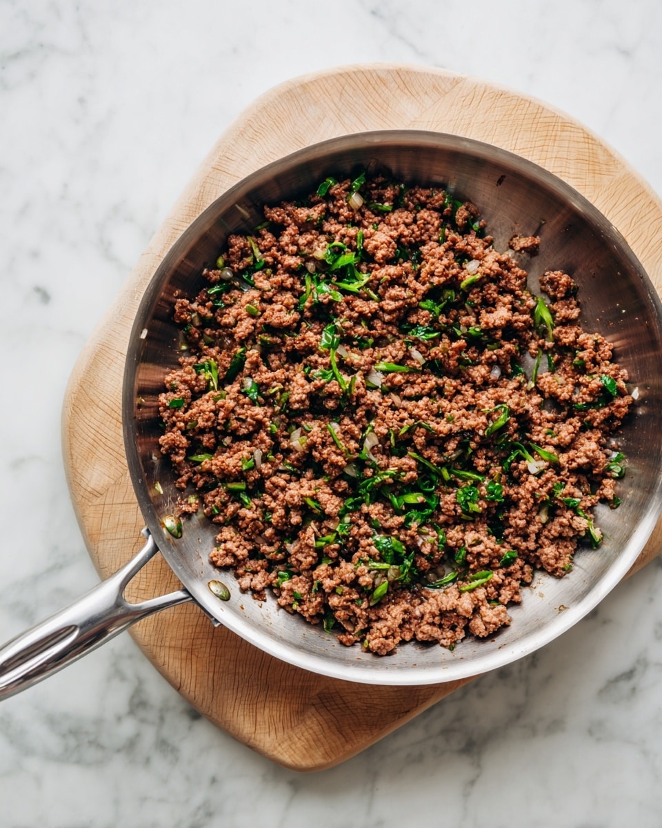 A silver pan with a long handle holds cooked ground meat mixed with small bits of green herbs and onion pieces. The meat is brown with hints of lighter and darker shades, showing a slightly crumbly texture inside the metal pan. The pan sits on a white wooden round board, and everything is placed on a white marbled surface. Photo taken with an iphone --ar 4:5 --v 7