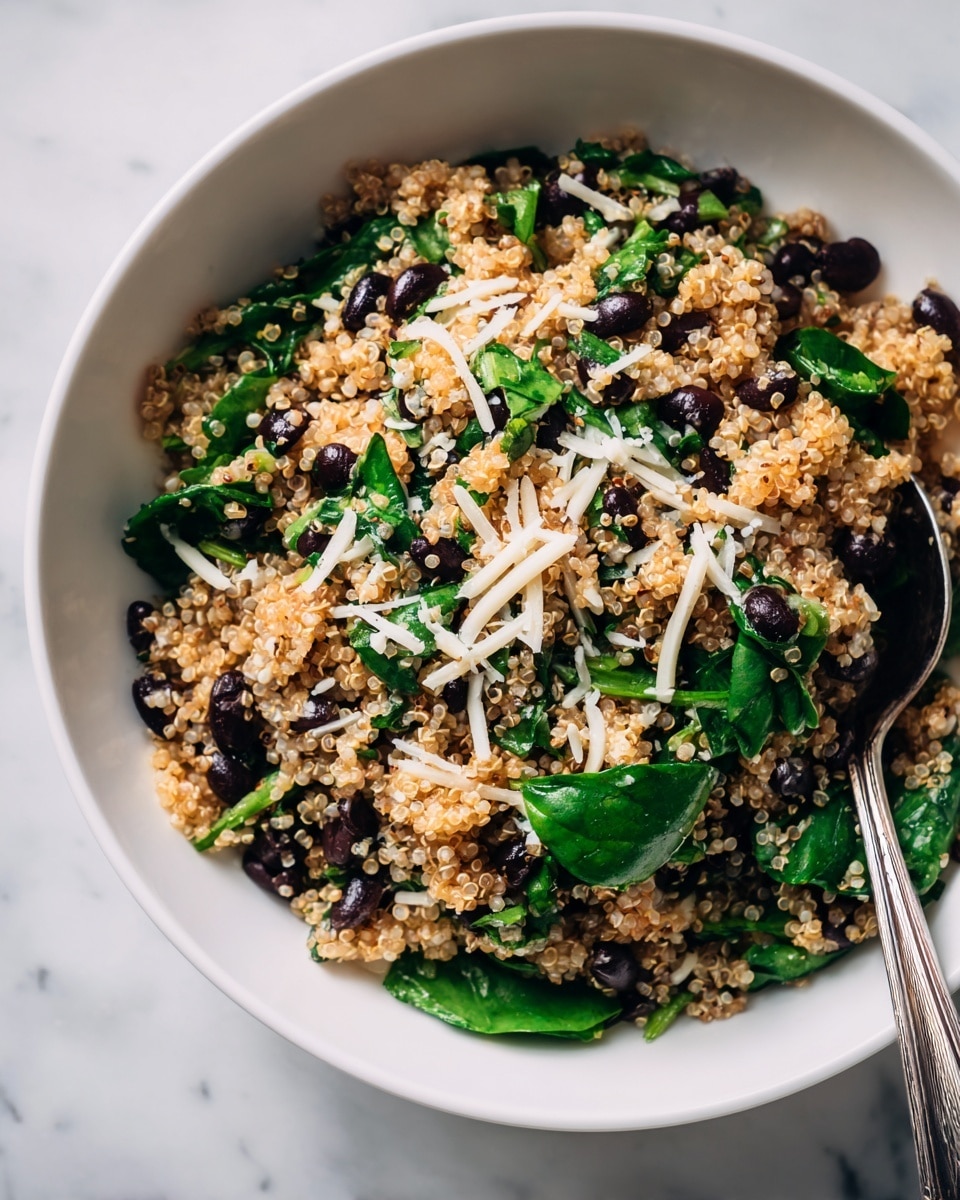 The image shows a close-up of a white bowl filled with a mixed salad. The salad has three main layers: a base of cooked, fluffy quinoa that is light brown in color, scattered with black beans that add a deep black contrast, and fresh green spinach pieces spread throughout. There are also thin strips of white cheese mixed evenly across the salad, adding texture. A silver spoon is partially visible on the right side inside the bowl. The bowl is placed on a white marbled surface. Photo taken with an iphone --ar 4:5 --v 7