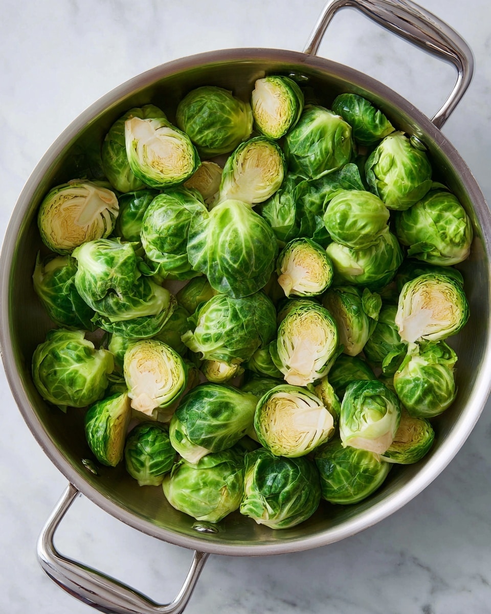 A stainless steel pan filled with halved Brussels sprouts that show layers of tightly packed green leaves with pale, almost white inner cores. The sprouts are scattered all over the pan, revealing different textures from smooth outer leaves to dense, fibrous inside layers. The pan sits on a white marbled surface, giving a clean and fresh look. The metal handles of the pan shine slightly under soft light, emphasizing the natural green color of the Brussels sprouts. Photo taken with an iphone --ar 4:5 --v 7