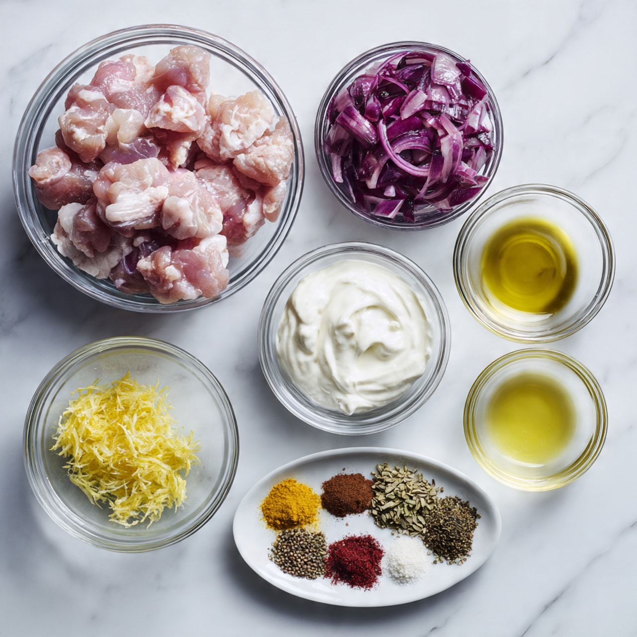 The image shows several clear glass bowls arranged on a white marbled surface. The largest bowl on the left is filled with raw pink chicken pieces with soft texture. To the top right, a medium bowl holds large chunks of purple-red onion with white layers inside. Below that is a bowl filled with thick white yogurt with a smooth texture. Near the center, a small bowl contains bright yellow lemon zest, and next to it is a small bowl with clear golden olive oil. At the bottom right, there is a smaller bowl with clear lemon juice. On the bottom left, a white plate holds various spices arranged in neat piles, featuring colors like red, black, green, brown, and white, each with a fine powder or small seed texture. Photo taken with an iphone --ar 4:5 --v 7